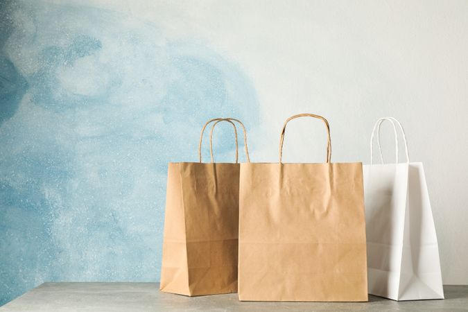 Paper bags on grey table against blue background, copy space