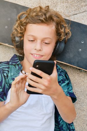 Cheerful preteen skater in headphones browsing smartphone on str