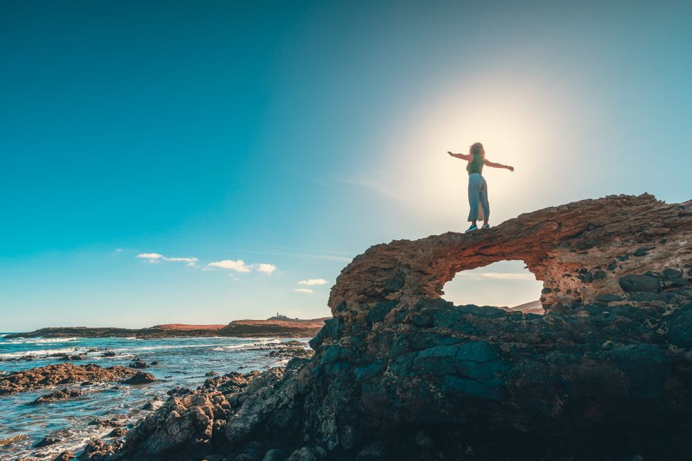 Anonymous woman with outstretched arms on cliff near sea