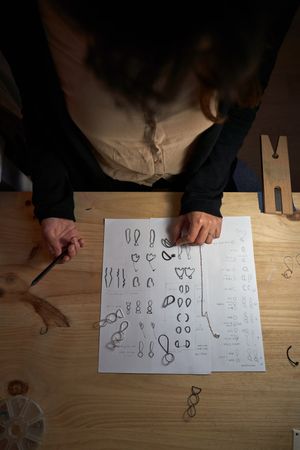 Crop goldsmith working on jewelry illustrations in dark studio