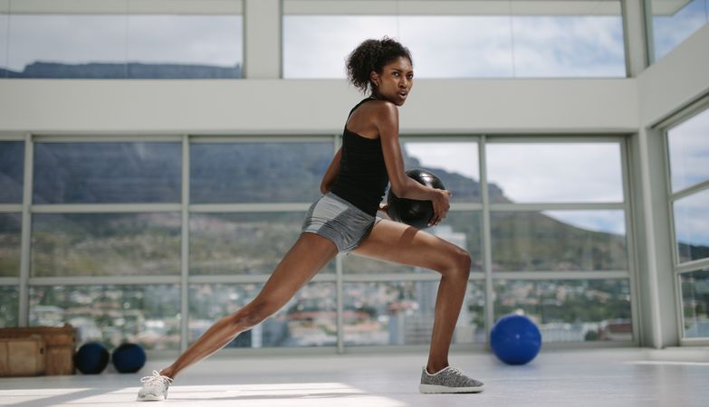 Black female doing stretching exercise with medicine ball