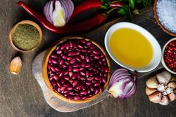 Top view of bowls of kidney beans, oil, pepper, garlic bulb and onions