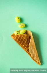 Waffle cone with green speckled eggs on green pastel background 5qkPv1