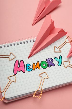 Vertical composition of notepad with “memory” written in colorful markers with paper planes, closeup
