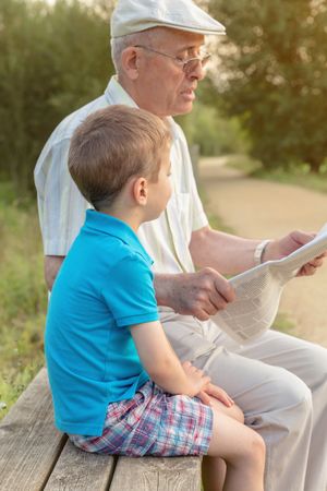 Older man and child reading a newspaper outdoors