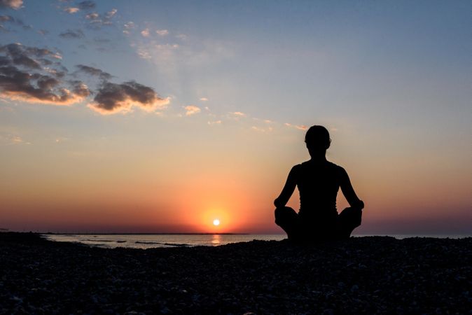 Silhouette of person meditating at the beach during sunset