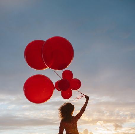 Cropped shot of female holding red balloons against a cloudy sunset sky