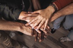 Diverse group of young people stacking hands together in a circle as a symbol of teamwork