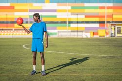 Black teenager with football ball against sky