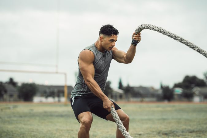 Strong man exercising with battle ropes on grass field