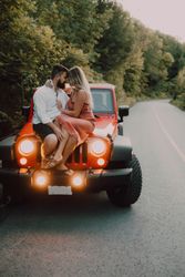 Loving couple sitting on car on road near forest