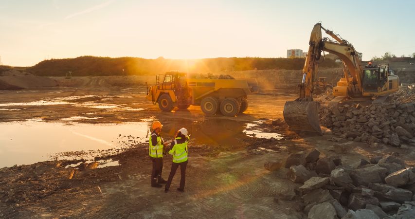 Aerial Drone Shot Of Construction Site On Sunny Evening: Industrial Excavators Digging Rocks And Loading Them Into Truck. Civil Engineer And Architect Observing Process, Discussing Real Estate Project