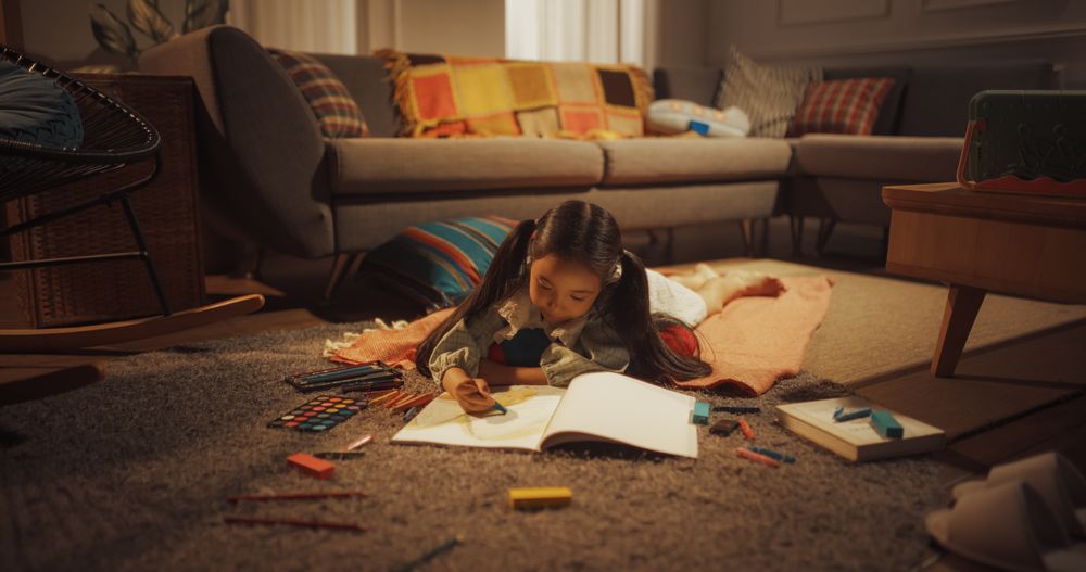 Evening Portrait of Cute Little Girl Drawing while Lying on the Floor in Living Room.