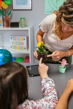 Female student pointing to a pansy roots holding by teacher hands in ecology classroom