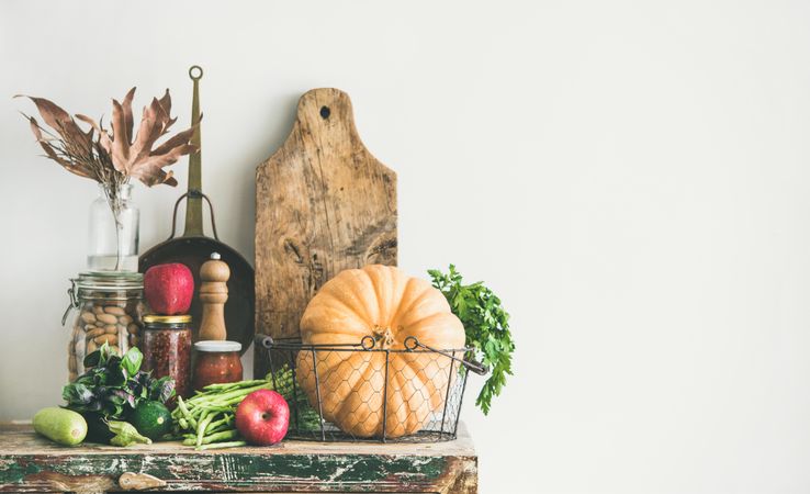 Fresh autumnal produce on kitchen counter, with squash and wooden board with apples, copy space