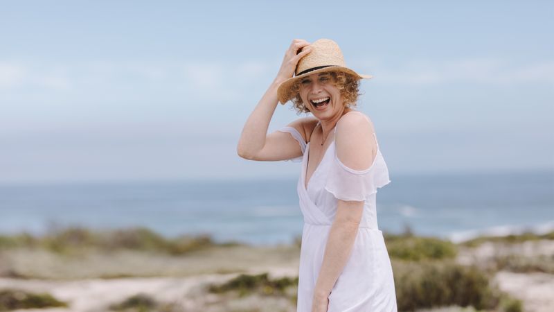 Portrait of a woman standing near sea wearing a hat