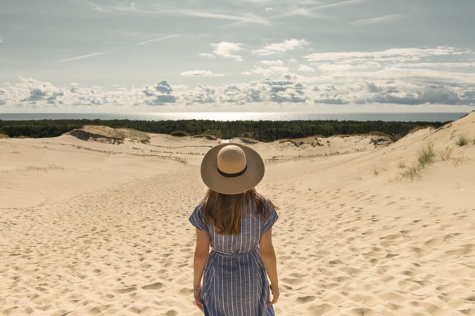 adult woman in casual dress and straw hat standing having good time on sand dune