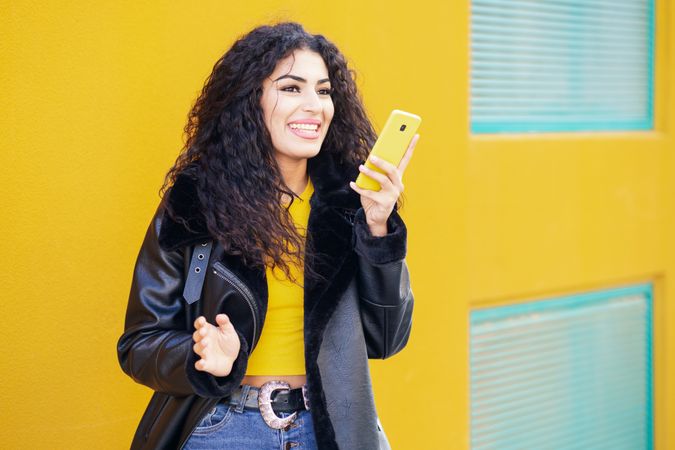 Female standing with yellow phone in front of yellow background with blue windows
