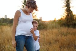 Pregnant mother and her son standing together in nature
