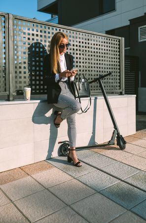 Businesswoman using mobile with her scooter next