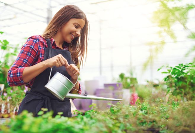 Smiling woman watering plants in a bright greenhouse