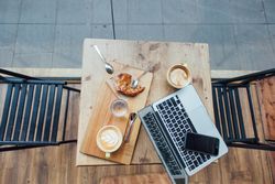 Top view of empty cafe table with laptop, pastry and cappuccinos