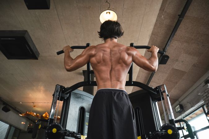 Muscular guy doing pull ups on exercise machine