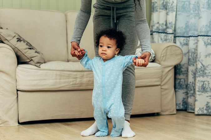 Toddler boy standing with the help of his mother