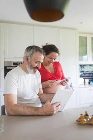 Smiling man and woman looking through book in kitchen