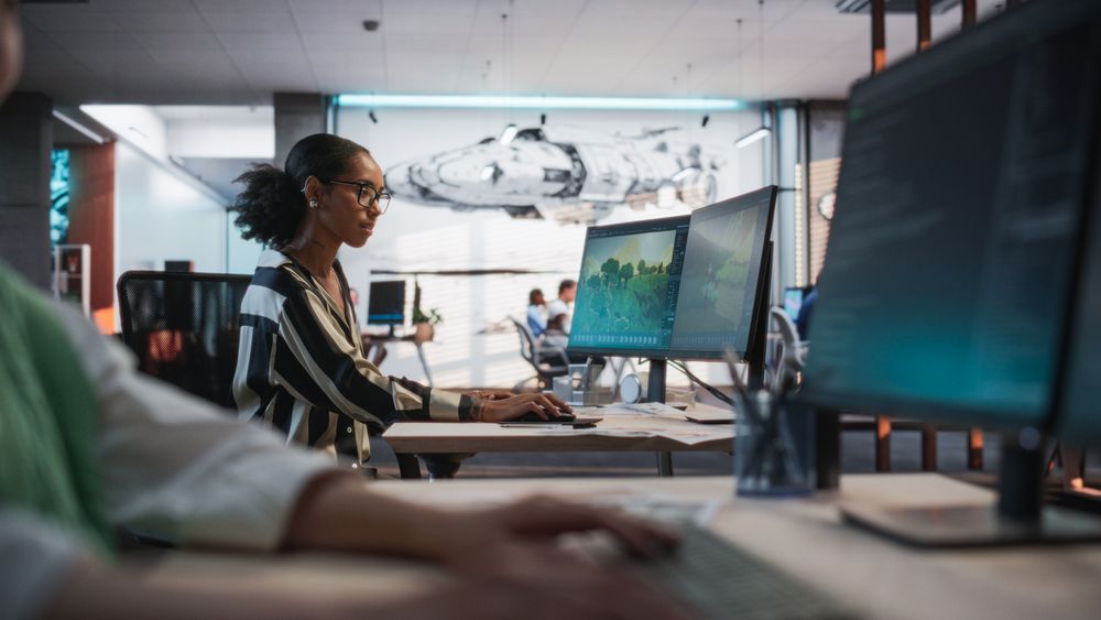 Black Female Game Developer Using Desktop Computer With 3D modelling Software And Talking to Asian Female Project Manager in Game Design Studio Office.