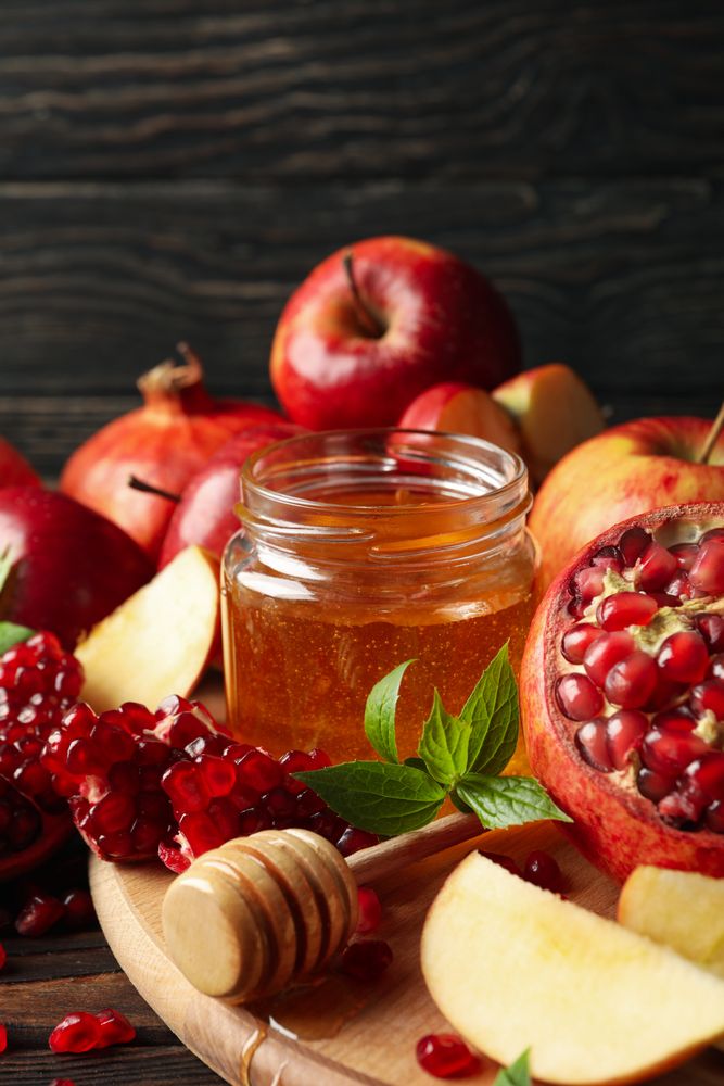 Apples on board with honey and pomegranate on dark wooden background, vertical