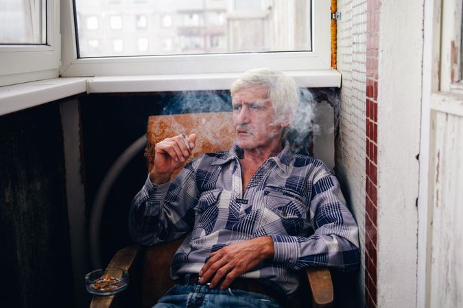 Older man smoking and sitting on chair looking away