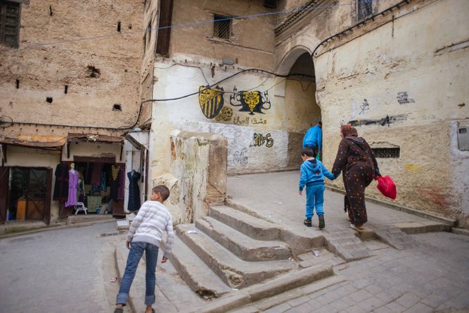 Mother walks her son up slanted cobblestone street with graffiti in Fez, Morocco