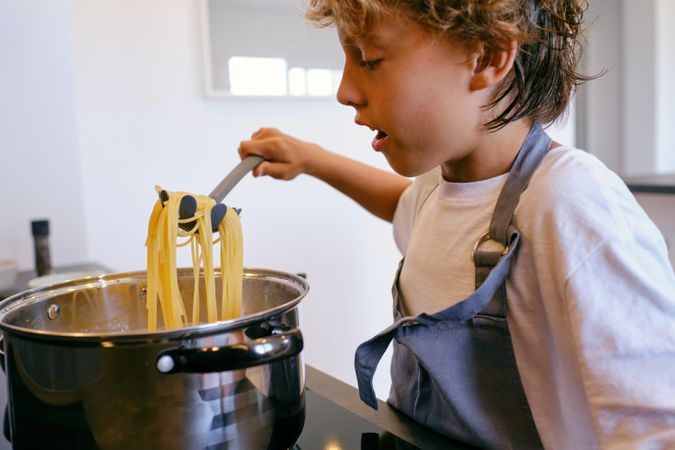 Crop boy cooking spaghetti in pot at home