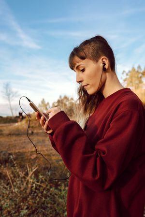 Young woman with piercing listening music on smartphone on hill