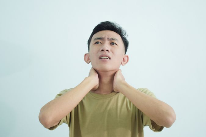 Asian young man touching neck in pain and wincing