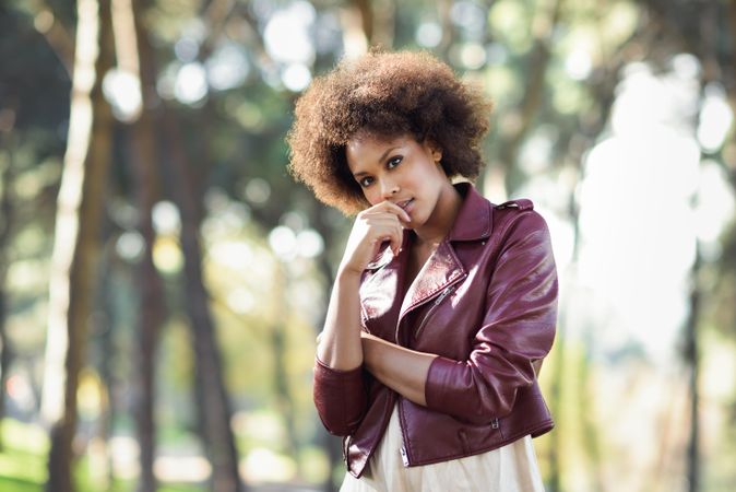 Woman standing in front of trees in red leather jacket and her hand to her face
