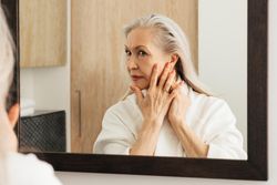 Female in bathrobe checking her skin in mirror