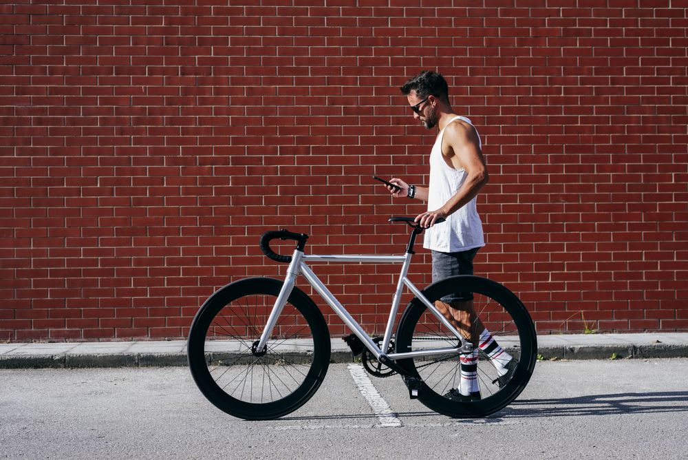 Sportive man with bicycle using phone