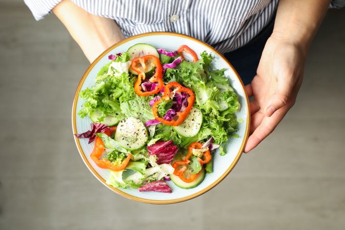 Young woman holding salad on wooden background, top view