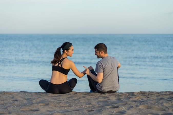 Happy couple in sportswear sitting on beach