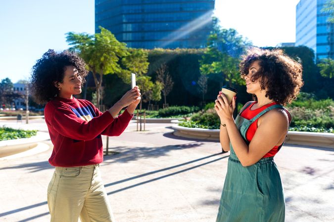 Woman taking photograph of a female friend with smart phone in the city