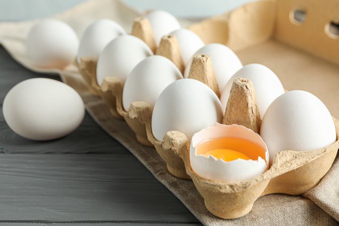 chicken eggs in carton box on wooden table, space for text and closeup