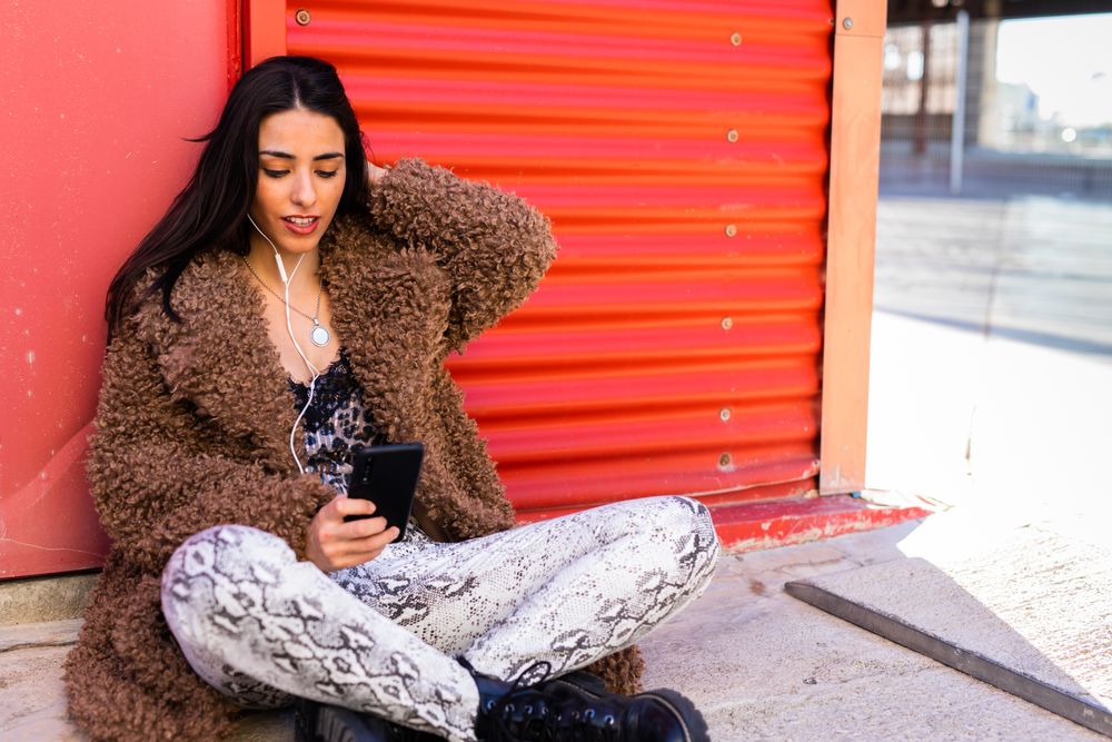 Trendy woman with smartphone near wall