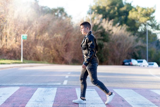 Side view of teenage male wearing a leather jacket walking on crosswalk