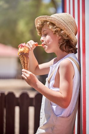 Cute boy in straw hat eating delicious ice cream with syrup