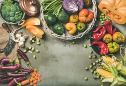 Fresh produce on concrete background, with thatched basket, halved squash, corn, with copy space