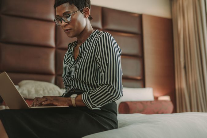 Woman in business wear sitting on bed in hotel room using laptop