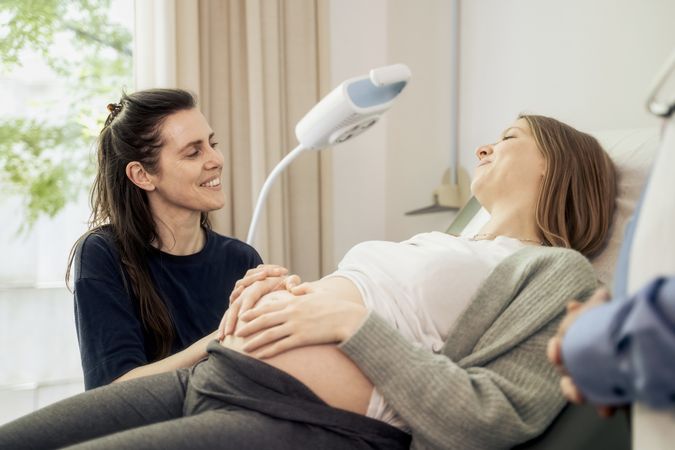 Tender moment between a lesbian couple at a pregnancy check-up.