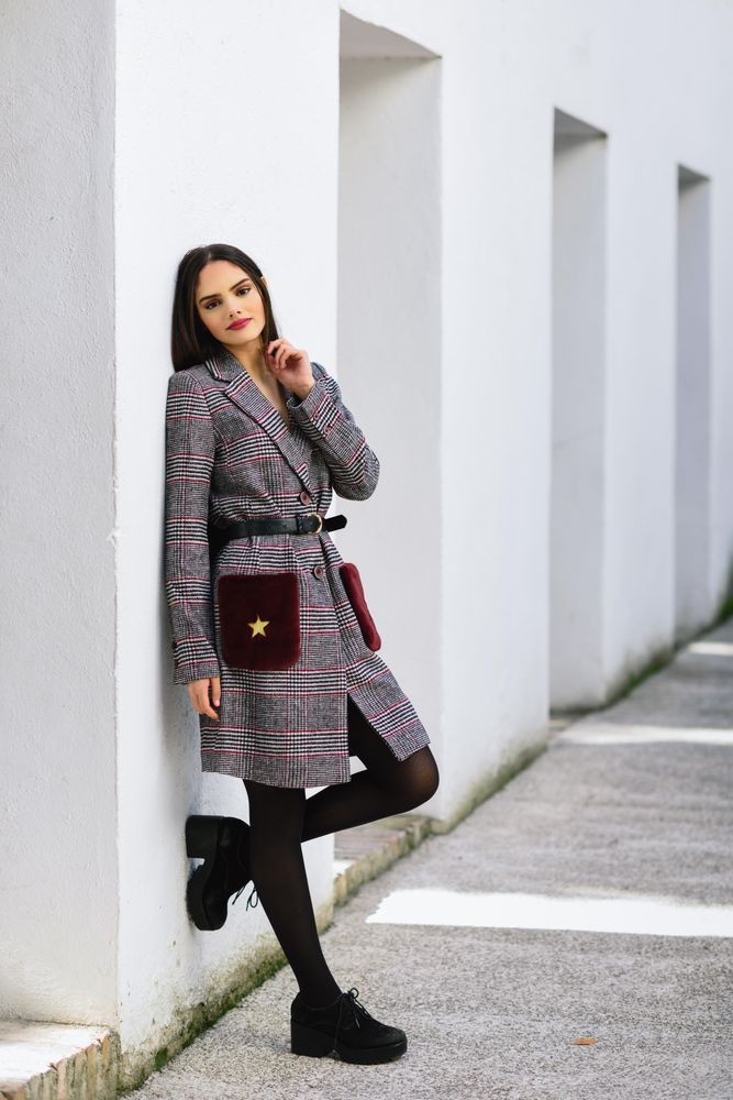 Female leaning on bright wall outside in winter coat dress